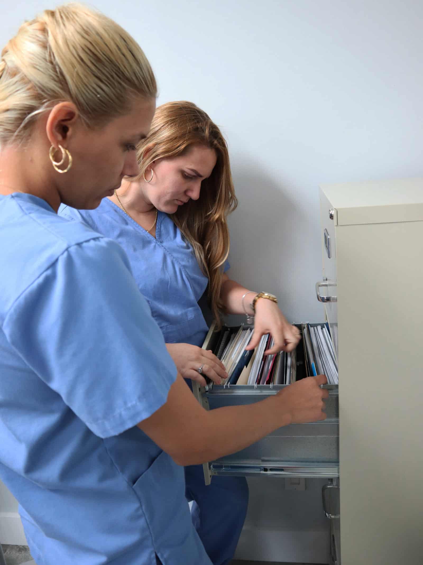 two Miami medical assistant training program students practice medical office management skills at a filing cabinet