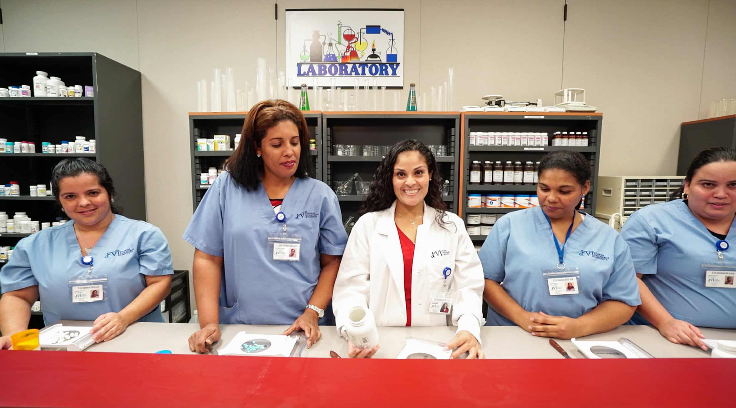 A pharmacy instructor smiling at the camera in the pharmacy lab with smiling miami pharmacy technician program students standing on either side of her