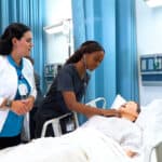 An FVI nursing instructor watches Miami and Miramar ASN nursing program students performs health checks on a patient simulator in a skills lab