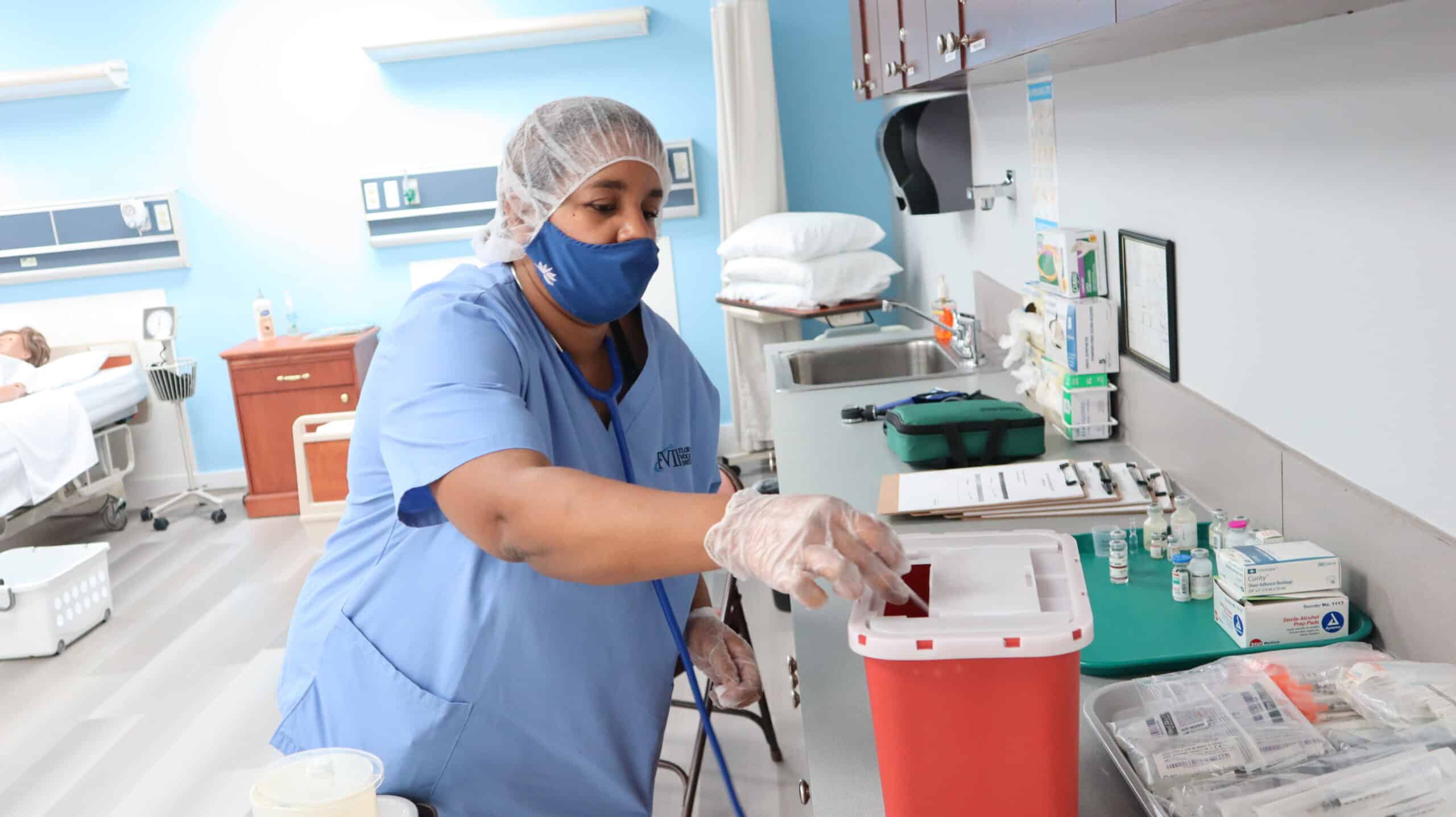 A Miramar medical assistant training program student safely disposes of medical waste in a biohazard collection container in a skills lab