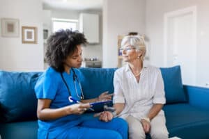 African Nurse Checking Senior Patient's Blood Pressure in the Livingroom. Female Doctor Measuring Blood Pressure of Senior Woman.