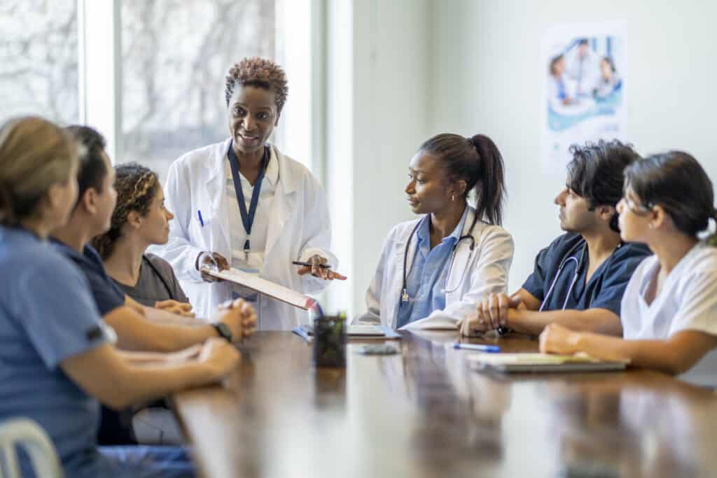 A small group florida nursing students sit around a boardroom table as they listen attentively to their teacher and lead doctor.