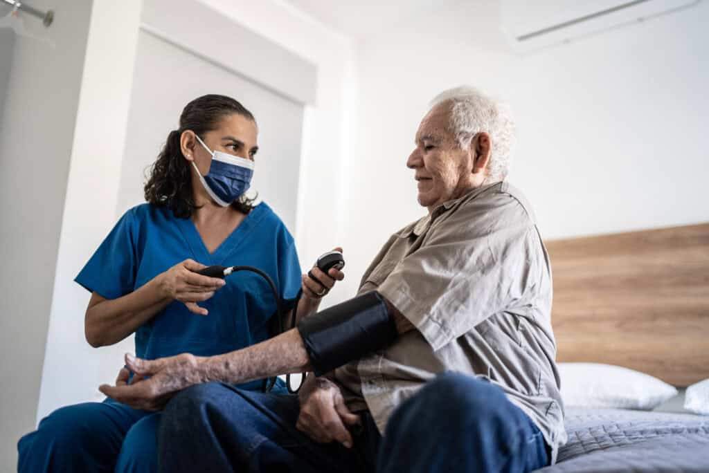 florida patient care technician taking pressure of senior man in the bedroom at his house