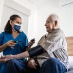 florida patient care technician taking pressure of senior man in the bedroom at his house