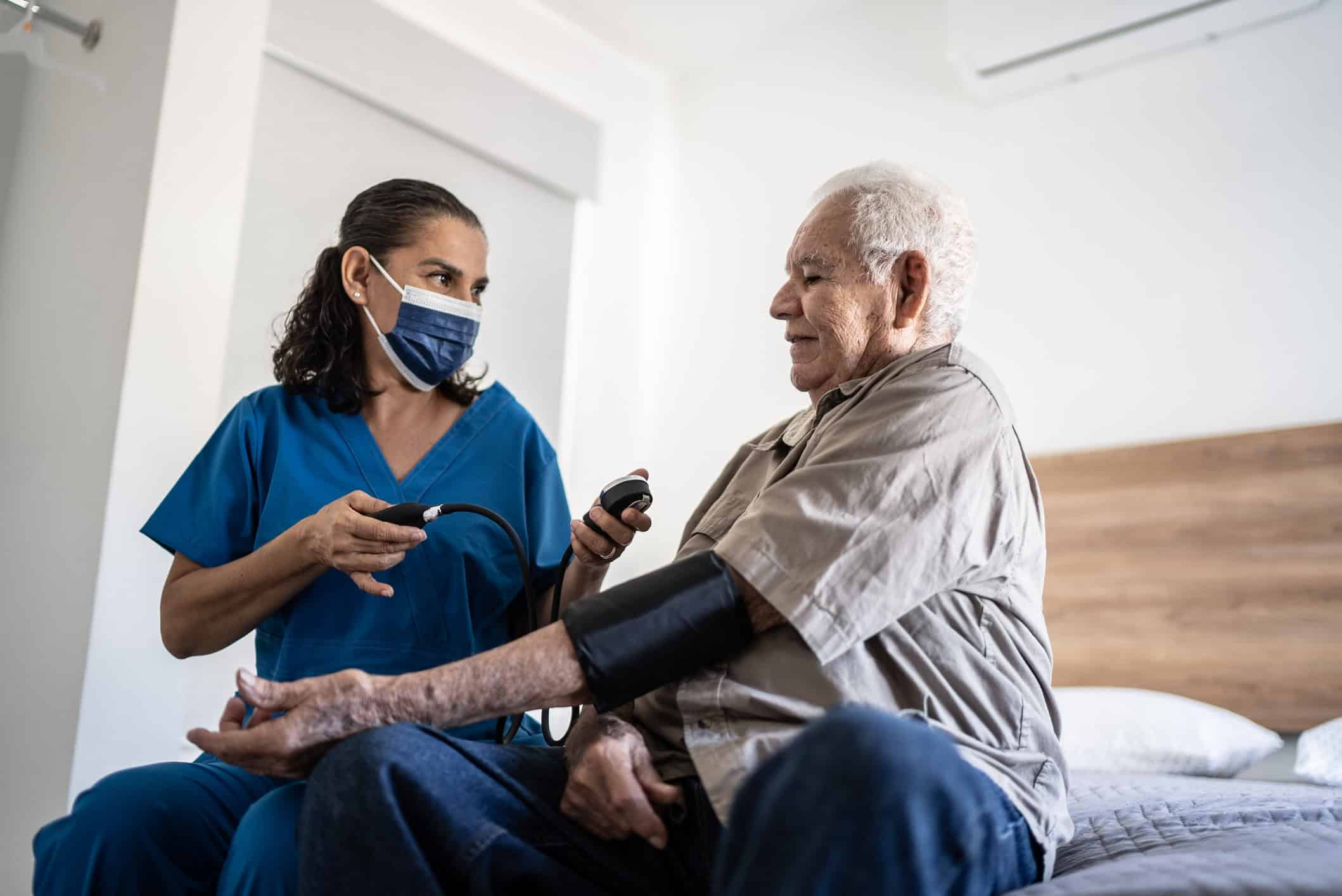 florida patient care technician taking pressure of senior man in the bedroom at his house