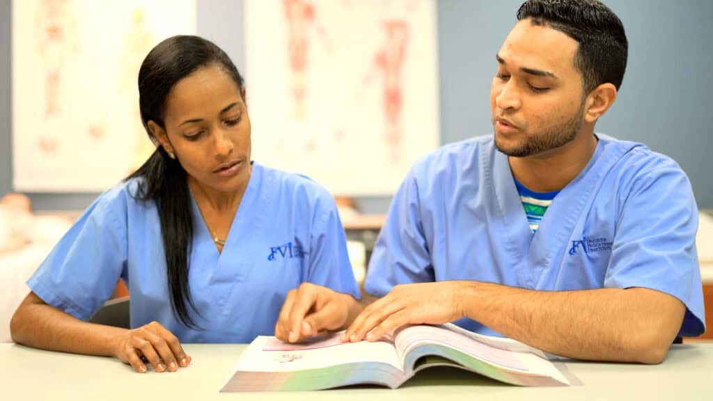 2 Miramar home health aide program students studying from a book in a classroom