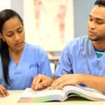 2 Miramar home health aide program students studying from a book in a classroom