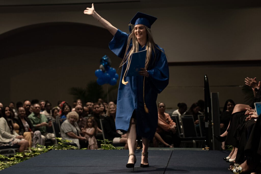 happy diploma program graduate walking down the stage during graduation