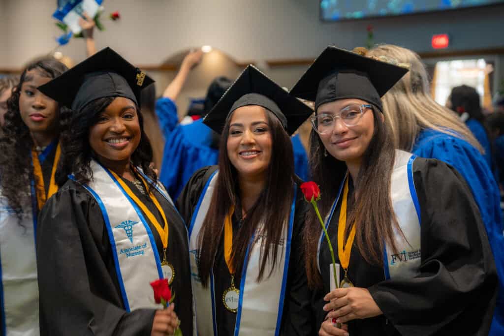 3 nursing graduates at graduation, 2 holding red roses