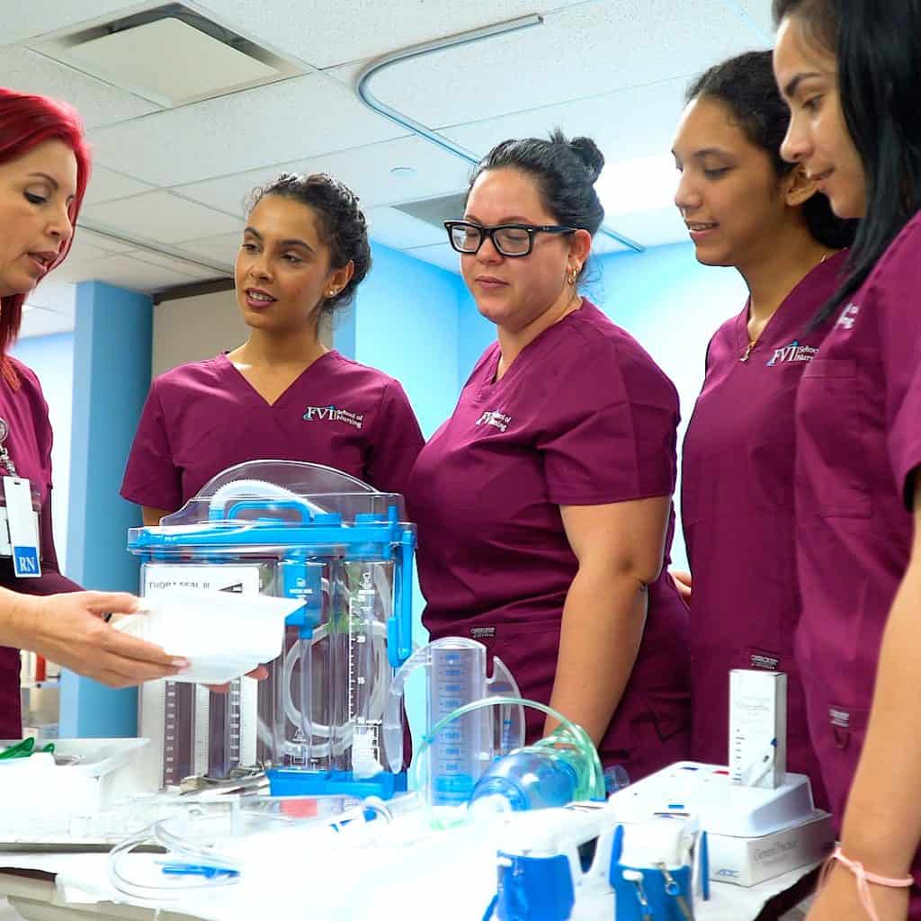 Practical Nursing program students in Miami learning from an RN instructor during a hands-on lab session with medical equipment.