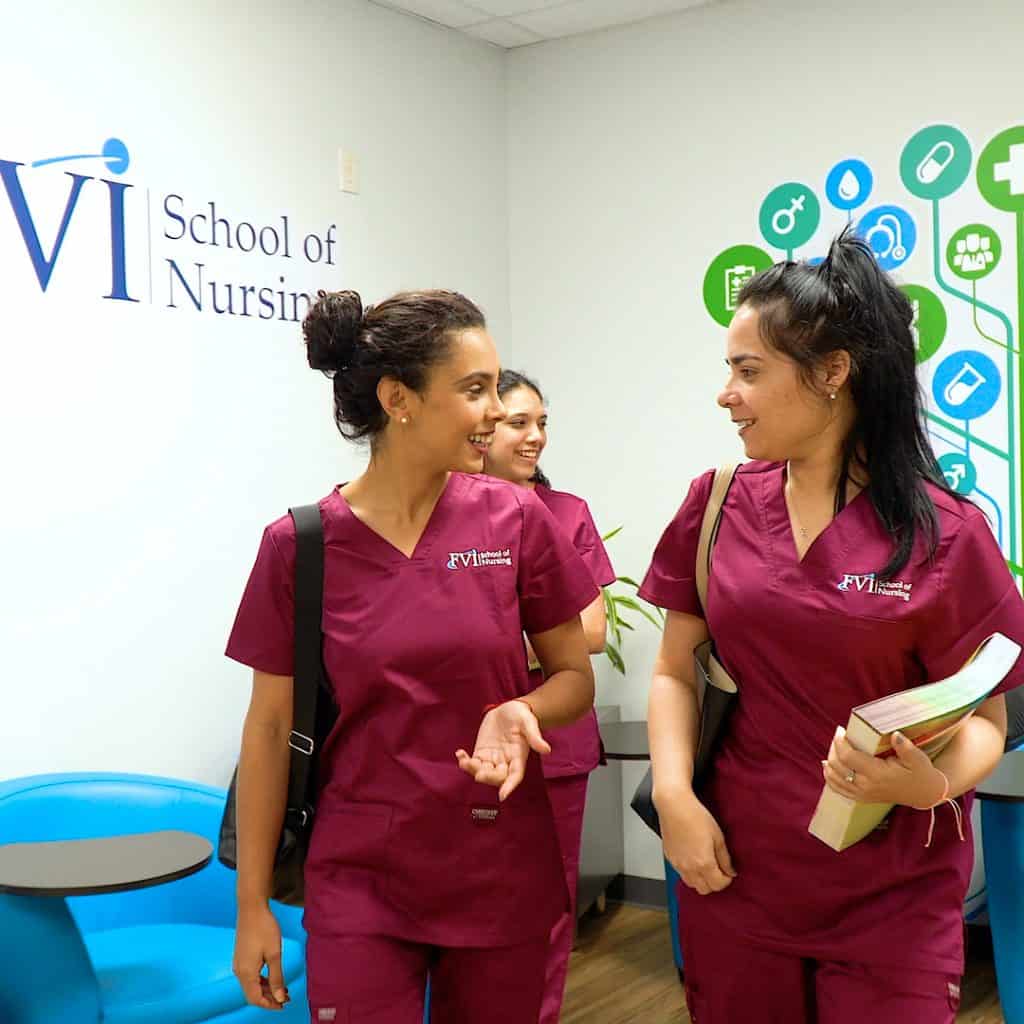Three Practical Nursing students in Miami smiling and talking at FVI School of Nursing, wearing burgundy uniforms.