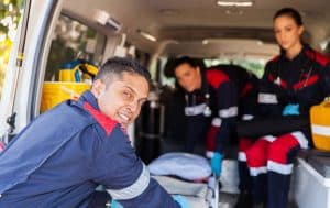 Smiling EMT professional standing in front of an ambulance with a stethoscope.