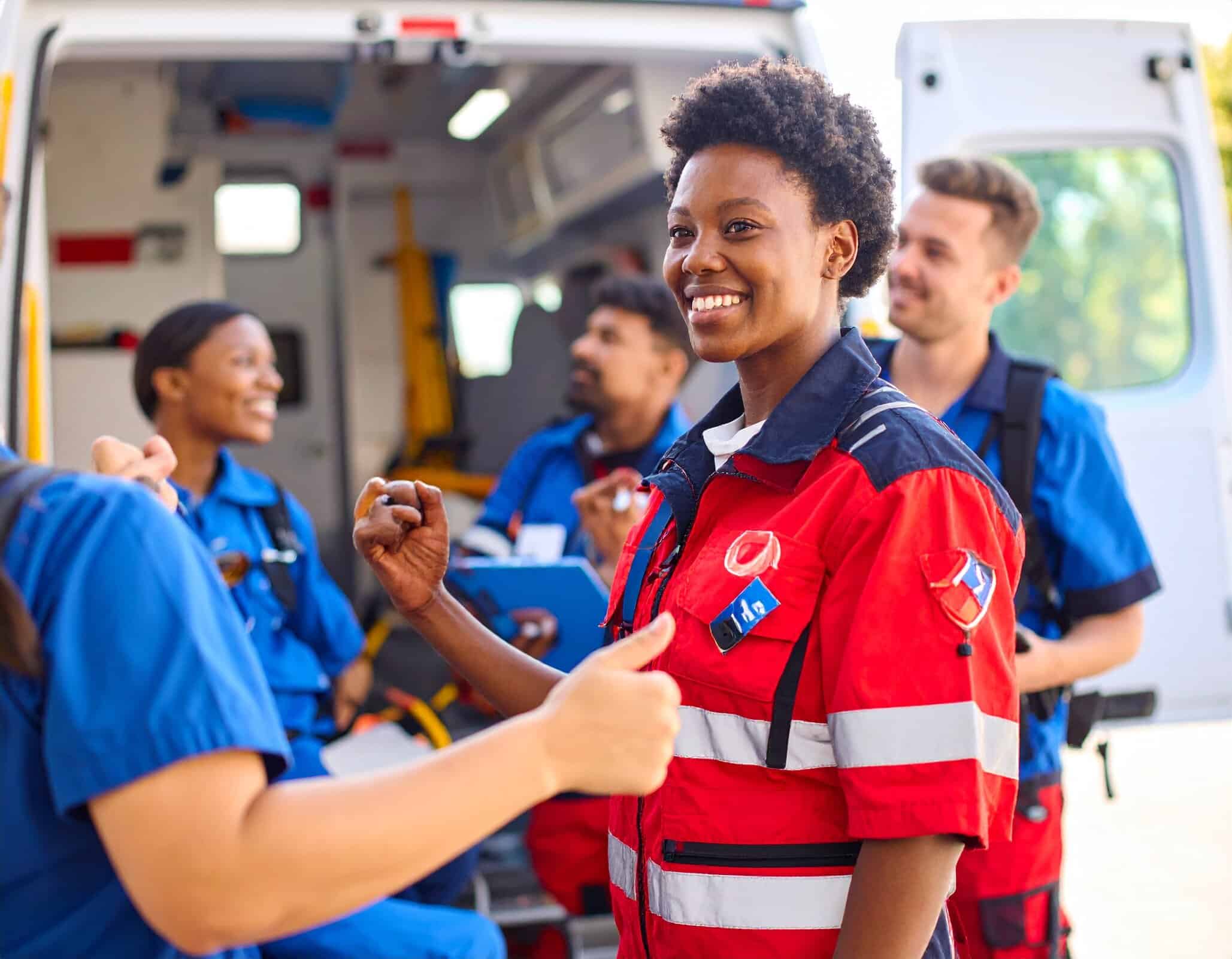 EMT students smiling and celebrating together outside an ambulance.