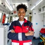 Confident EMT professional standing inside an ambulance with arms crossed.