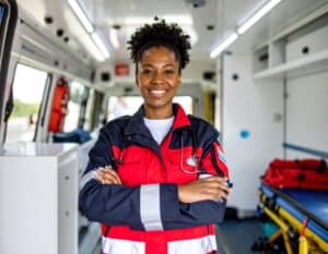 Smiling EMT professional standing in front of an ambulance with a stethoscope.
