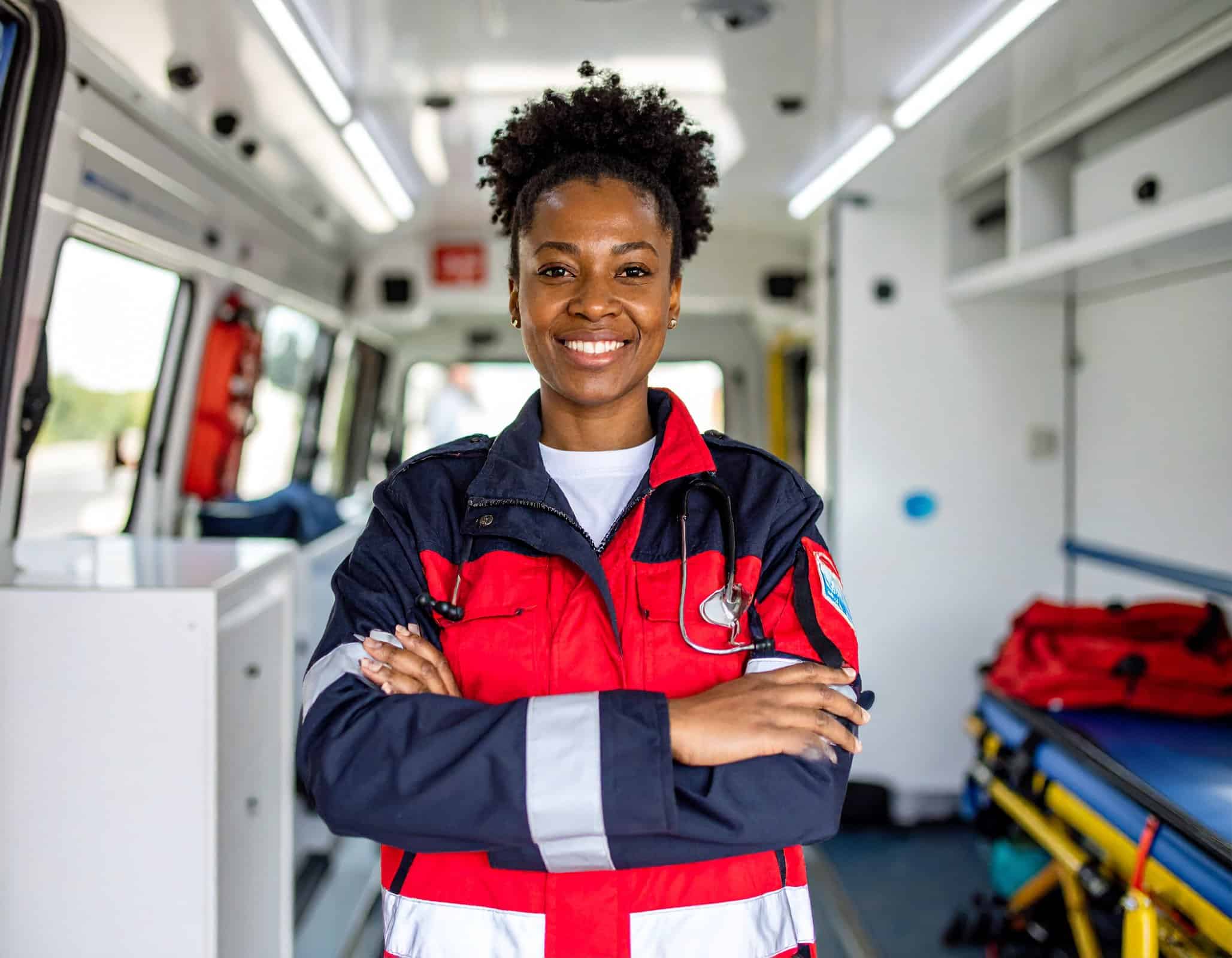Confident EMT professional standing inside an ambulance with arms crossed.